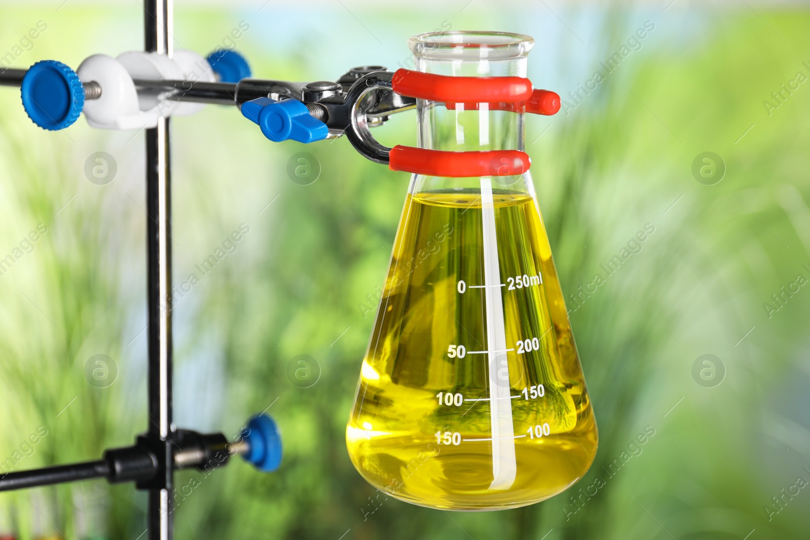 Photo of Retort stand and laboratory flask with liquid on blurred background, closeup