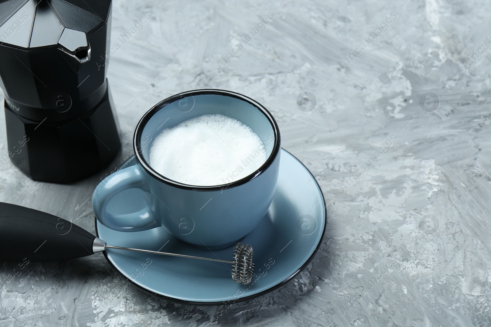 Photo of Mini mixer (milk frother), whipped milk in cup and moka pot on grey textured table. Space for text