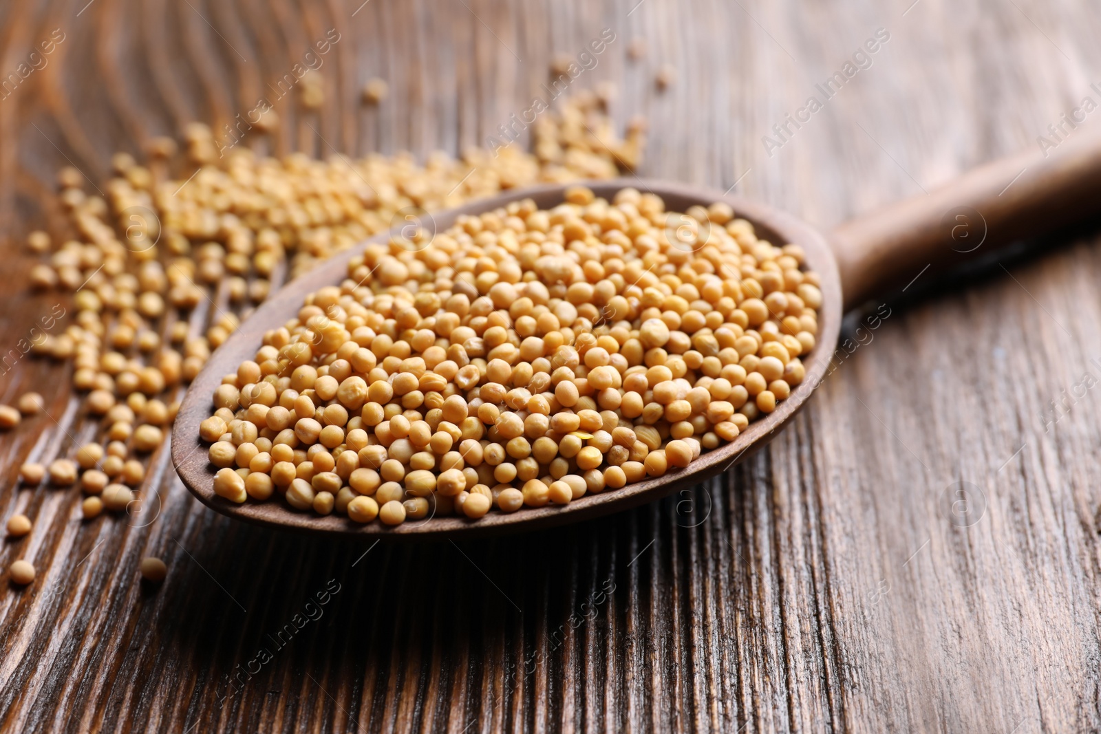 Photo of Mustard seeds in spoon on wooden table, closeup