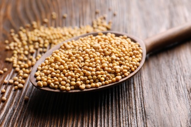 Photo of Mustard seeds in spoon on wooden table, closeup