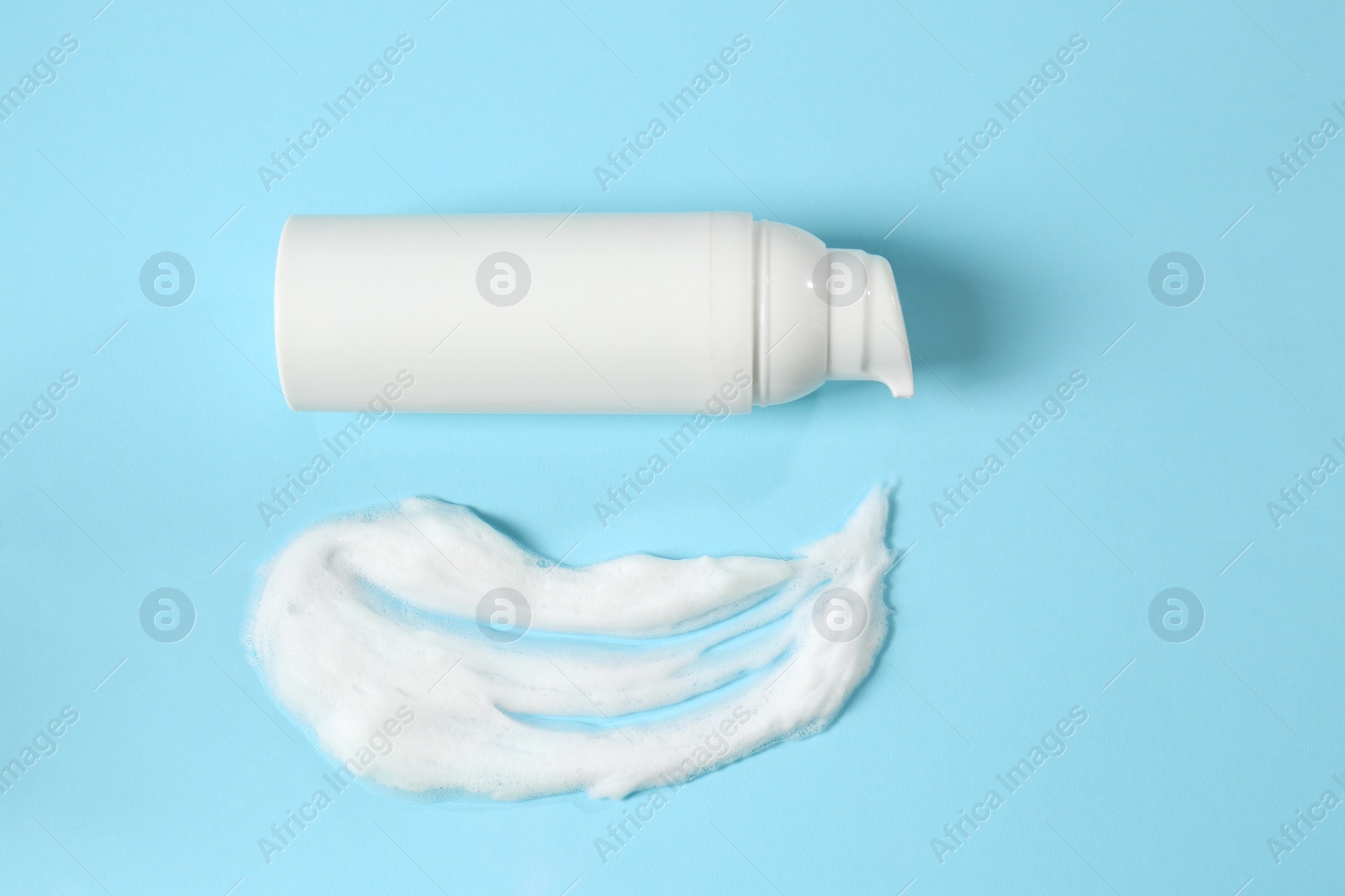 Photo of Bottle of face cleanser and white foam on light blue background, top view. Skin care cosmetic