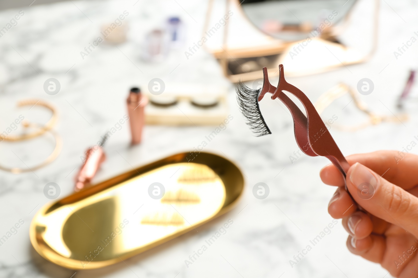 Photo of Woman holding tweezers with magnetic eyelashes at white table, closeup