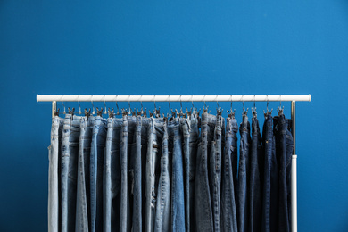 Photo of Rack with stylish jeans on blue background