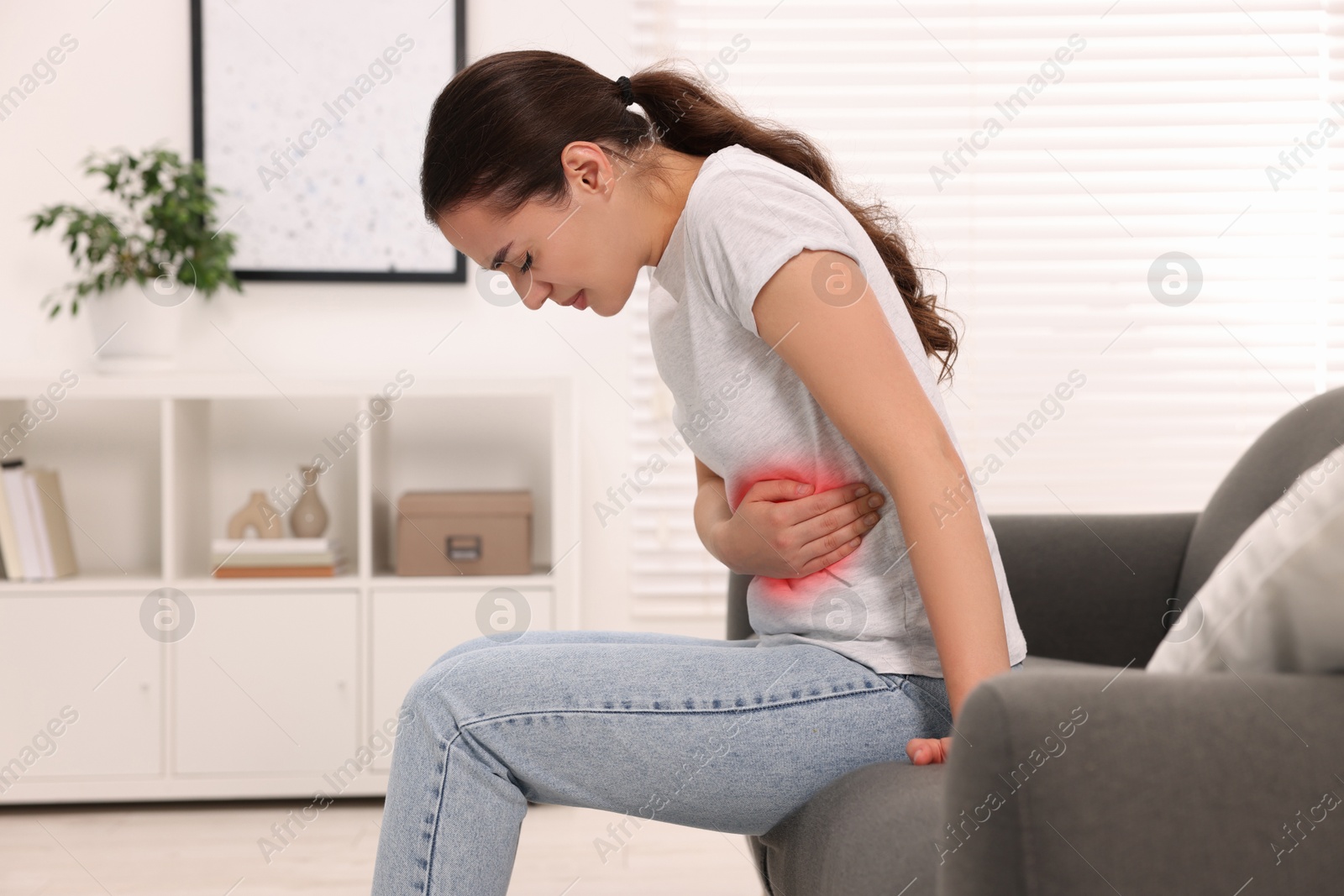 Image of Woman suffering from abdominal pain on sofa at home