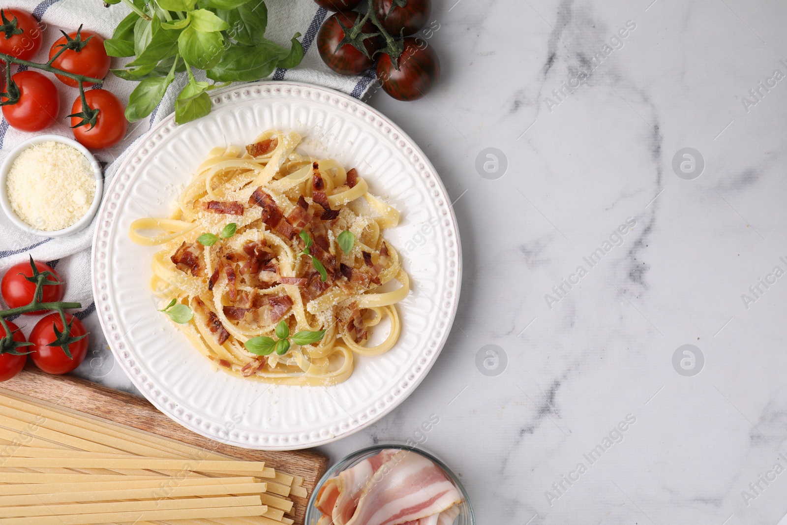 Photo of Tasty pasta with bacon and basil on white marble table, flat lay. Space for text