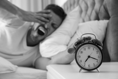 Image of Sleepy man turning off alarm clock at home in morning, selective focus. Black and white photography