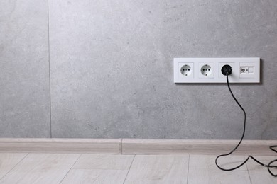 Photo of Power sockets and electric plug on grey wall, space for text