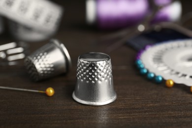 Photo of Silver thimble near sewing tools on wooden table, closeup