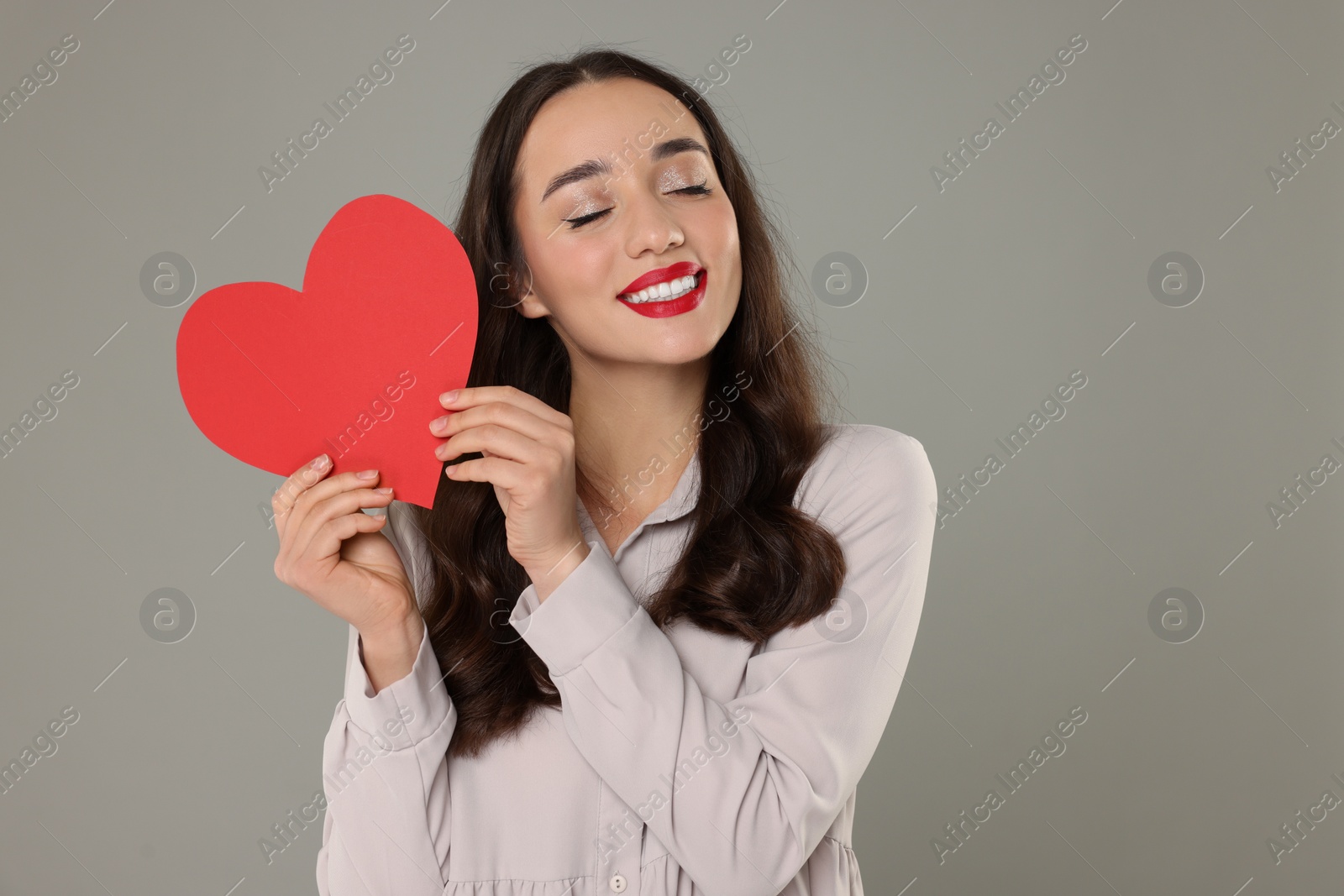 Photo of Beautiful young woman with paper heart on grey background, space for text