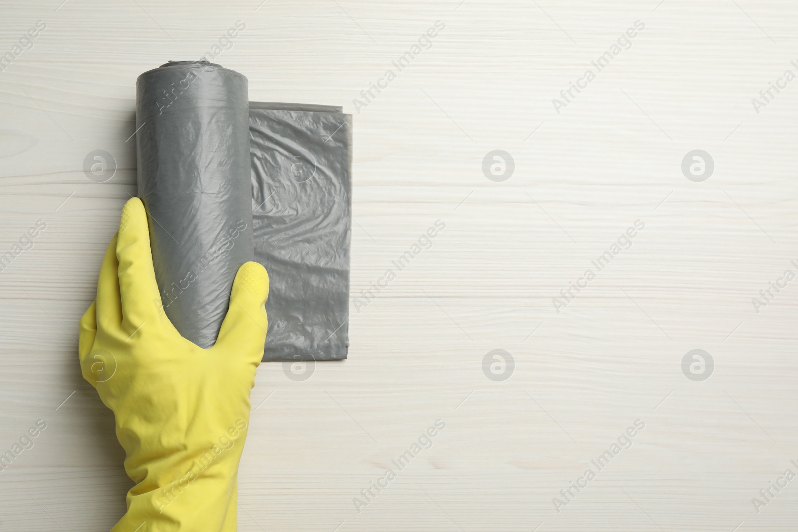 Photo of Janitor in rubber glove holding roll of grey garbage bags on white wooden table, top view. Space for text