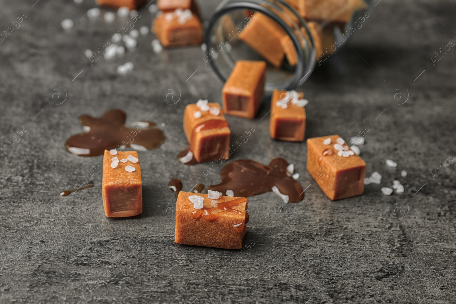 Photo of Delicious caramel candies with sauce and salt on gray background