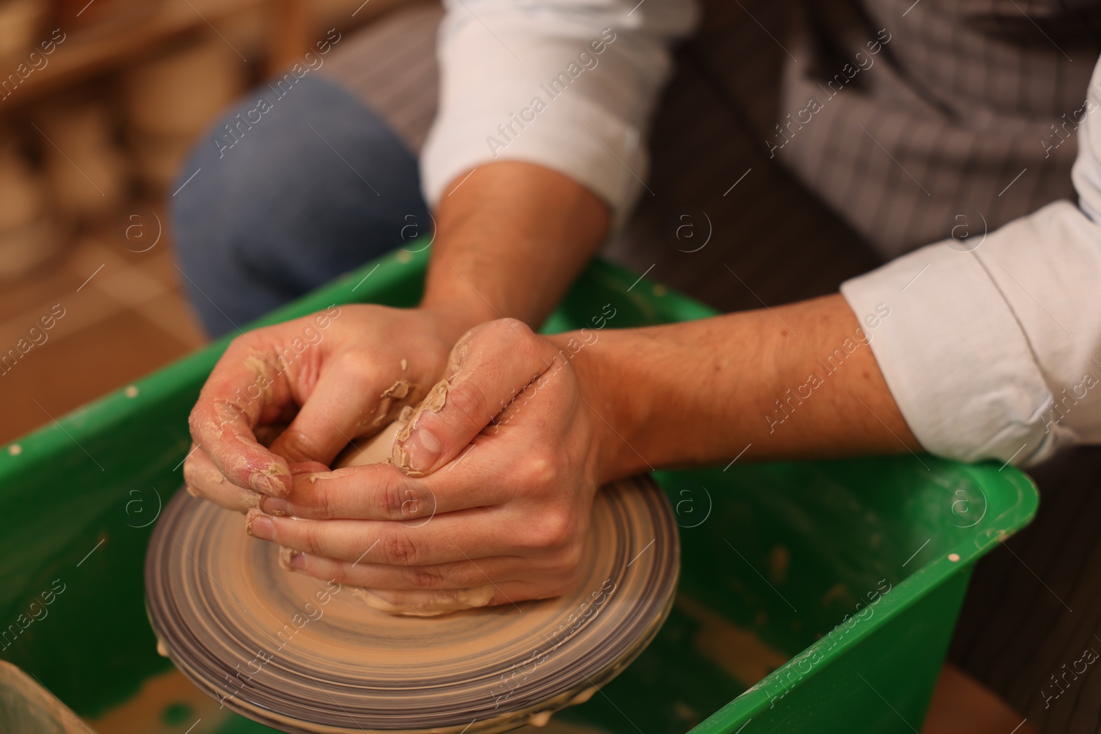 Photo of Man crafting with clay on potter's wheel indoors, closeup