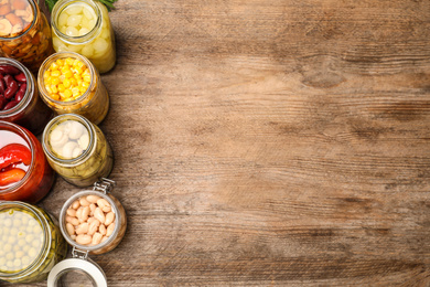 Photo of Glass jars with different pickled vegetables on wooden table, flat lay. Space for text