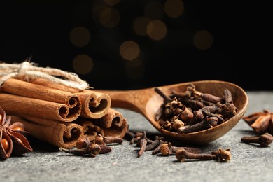 Photo of Wooden spoon with different spices on gray table against black background, closeup
