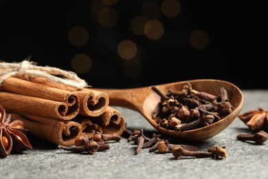 Wooden spoon with different spices on gray table against black background, closeup