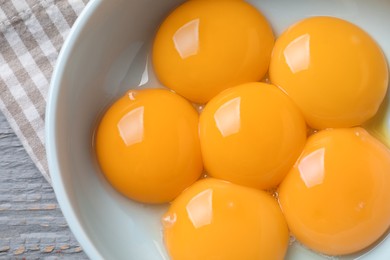 Bowl with raw egg yolks on grey wooden table, top view