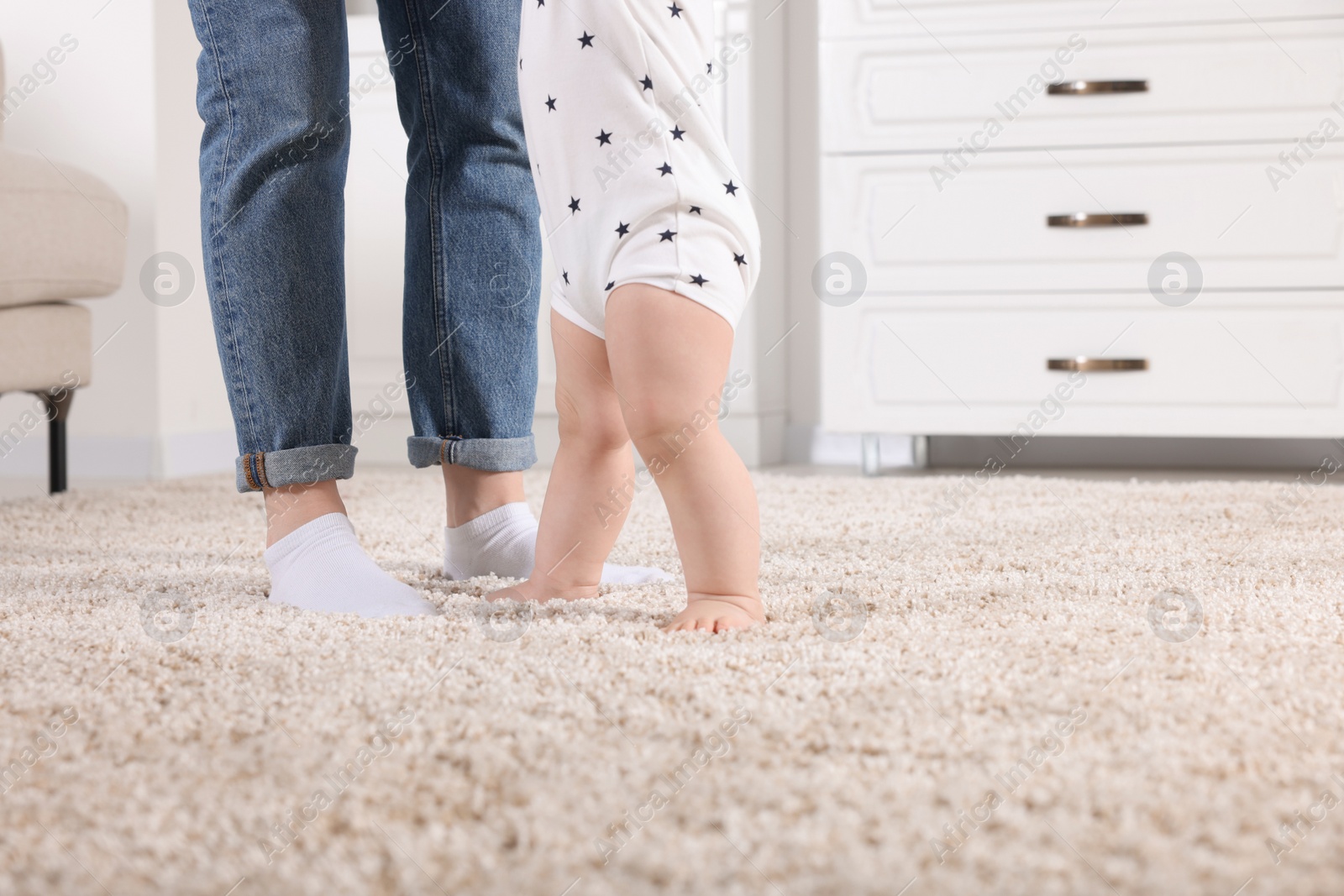 Photo of Mother supporting her baby son while he learning to walk on carpet at home, closeup. Space for text