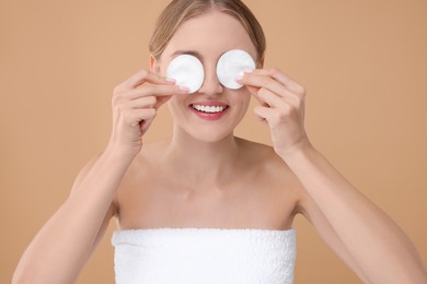 Young woman covering her eyes with cotton pads on beige background