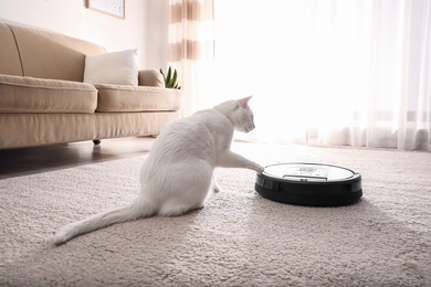 Photo of Modern robotic vacuum cleaner and cute cat on floor indoors