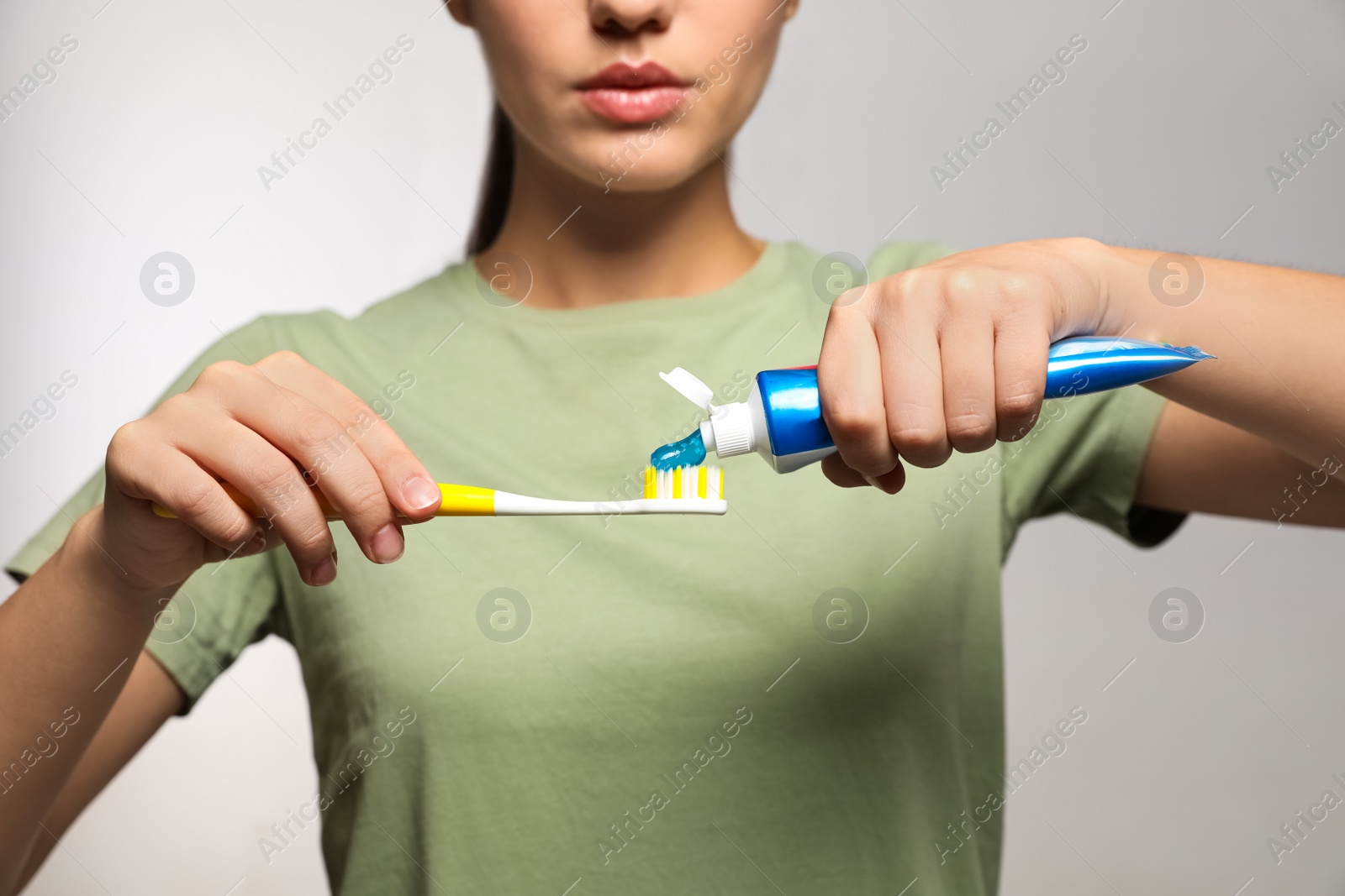 Photo of Woman applying toothpaste on brush against light background, closeup