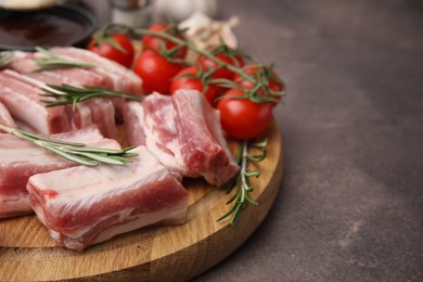 Photo of Cut raw pork ribs with rosemary and tomatoes on brown table, closeup. Space for text