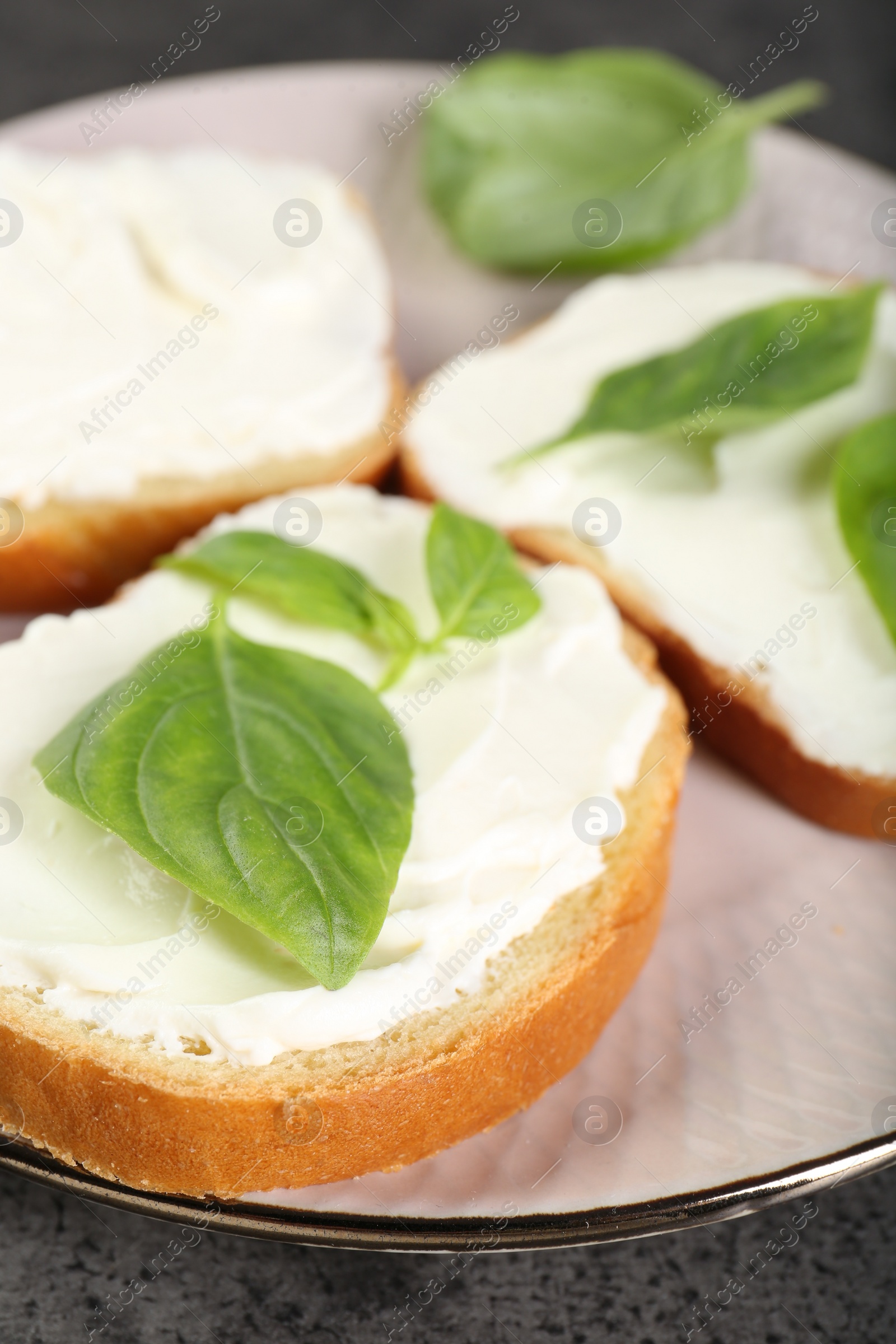 Photo of Delicious sandwiches with cream cheese and basil leaves on grey table, closeup