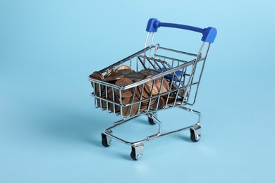 Photo of Small metal shopping cart with coins on light blue background