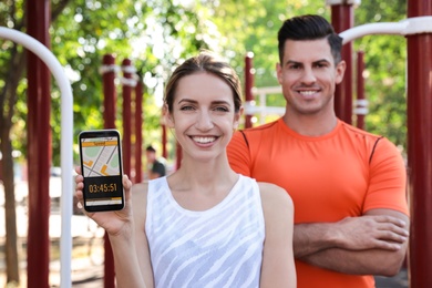 Photo of Couple showing smartphone with fitness app on sports ground