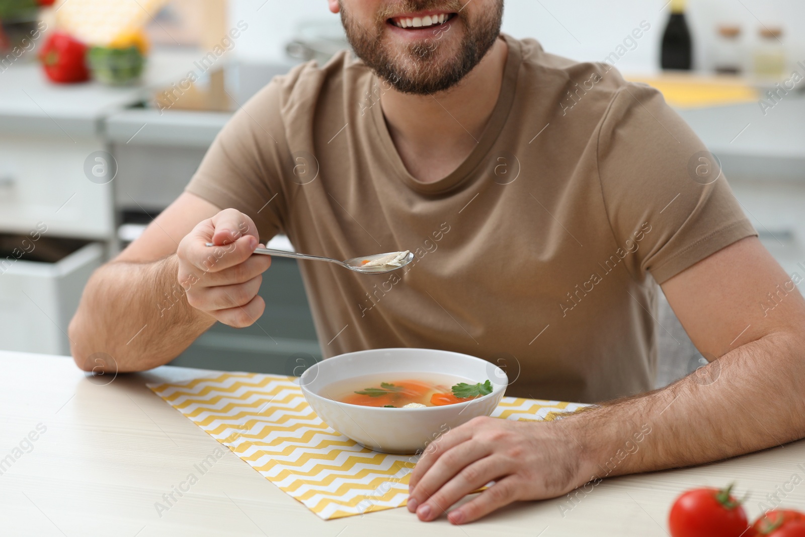 Photo of Young man eating tasty vegetable soup at table in kitchen, closeup