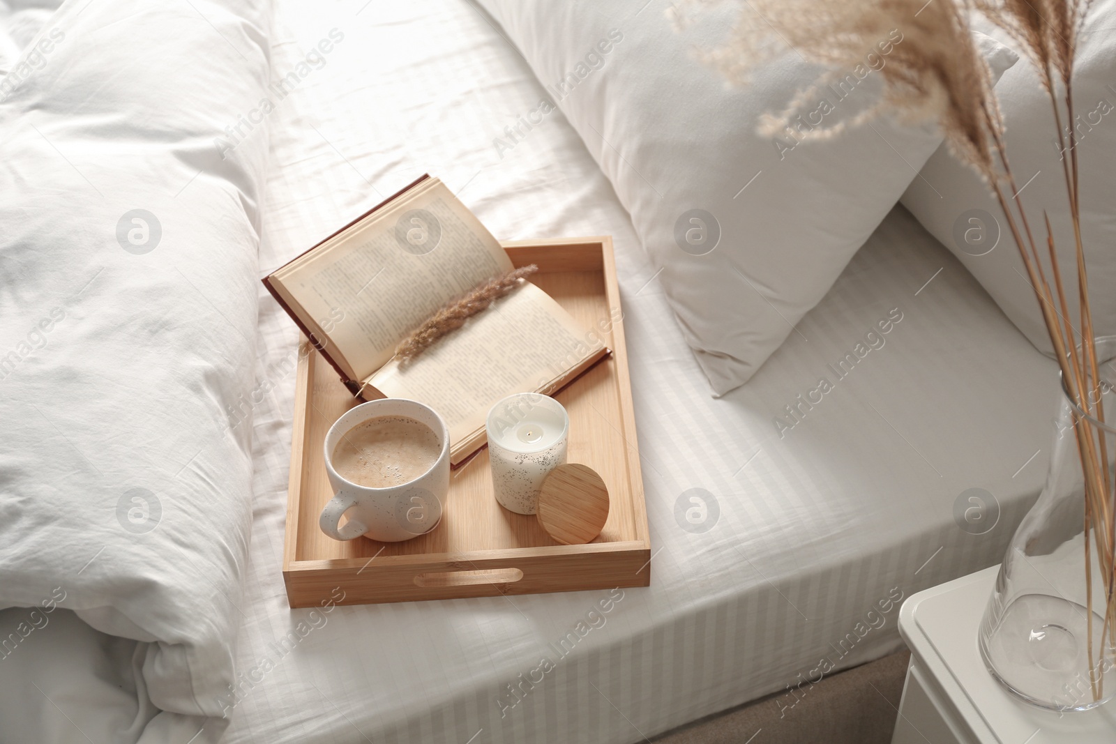 Photo of Cup of aromatic coffee, book and candle on bed with soft blanket indoors