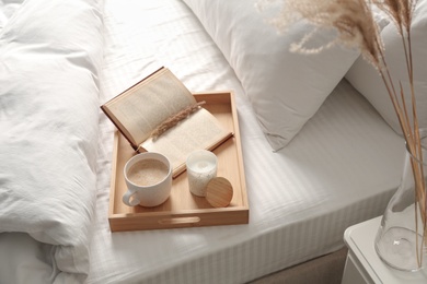 Cup of aromatic coffee, book and candle on bed with soft blanket indoors