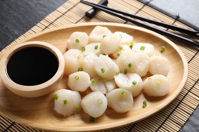 Photo of Raw scallops with green onion and soy sauce on dark table, closeup