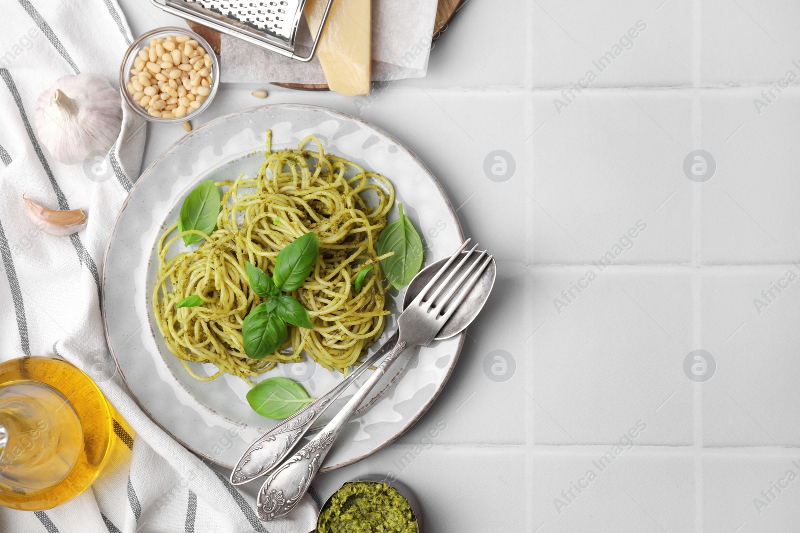 Photo of Delicious pasta with pesto sauce and basil served on white tiled table, flat lay. Space for text