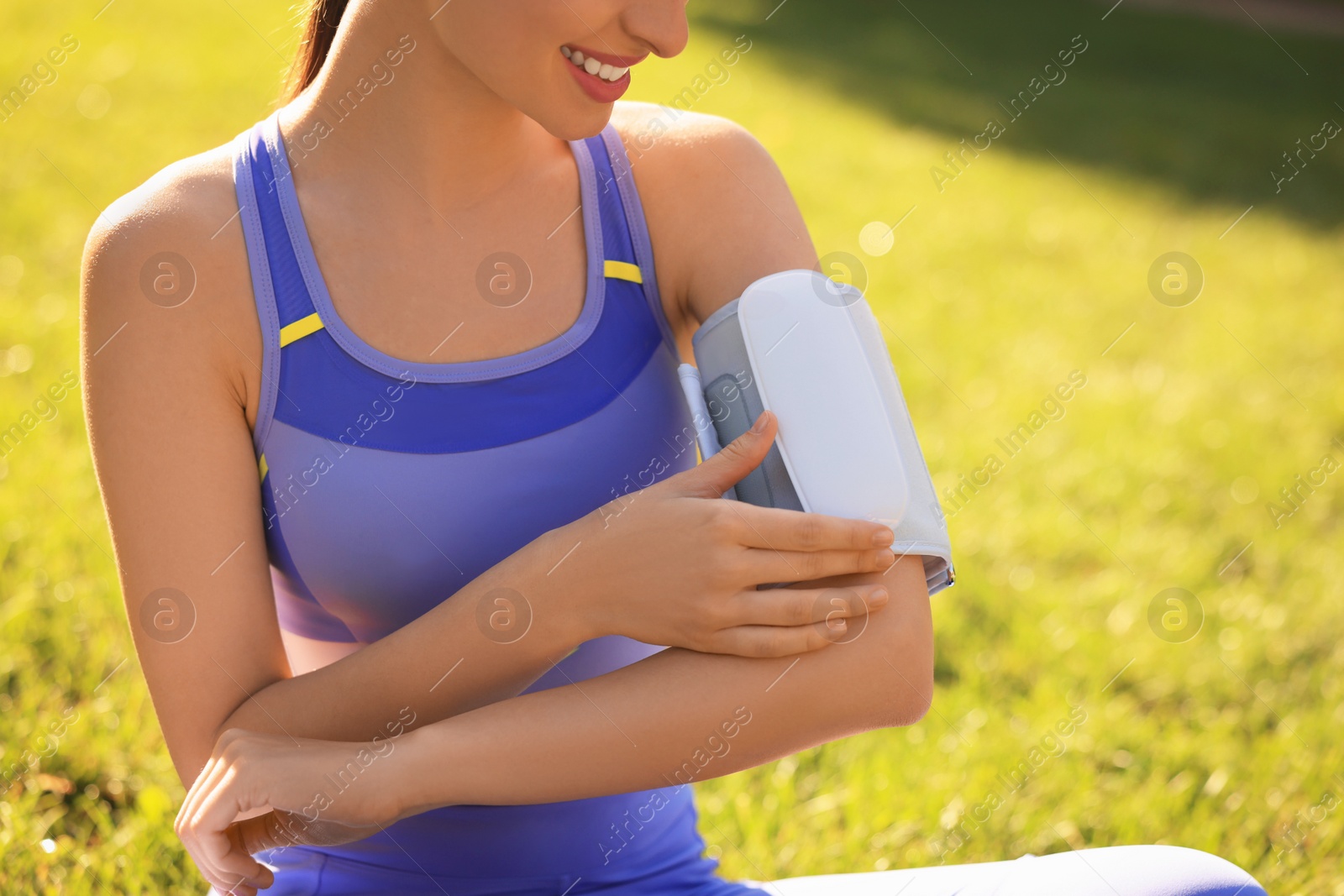 Photo of Woman checking blood pressure with modern monitor after training on sunny day, closeup. Space for text