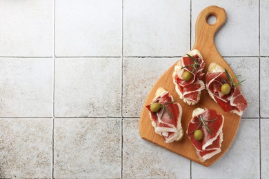 Photo of Tasty sandwiches with cured ham, rosemary and olives on tiled table, top view. Space for text