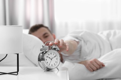 Photo of Young man turning off alarm clock at home in morning, focus on hand. Space for text