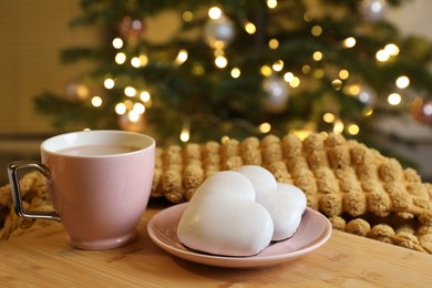 Photo of Cup of delicious cocoa and cookies on wooden table against blurred Christmas tree with lights