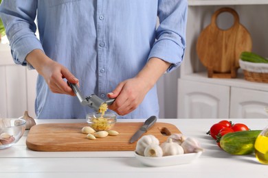 Photo of Woman squeezing garlic with press at white wooden table in kitchen, closeup