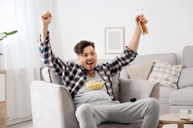 Photo of Lazy man with bottle of beer and chips watching TV at home