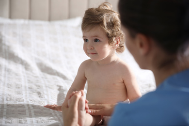 Photo of Orthopedist examining cute little baby on bed