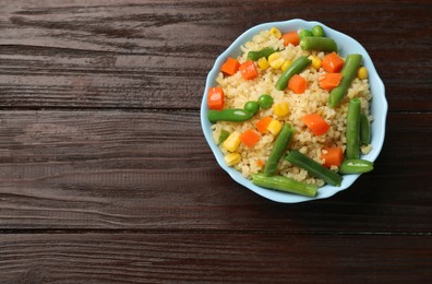 Photo of Delicious bulgur with vegetables in bowl on wooden table, top view. Space for text