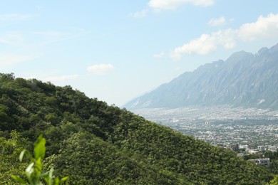 Picturesque view of mountains, city and trees under cloudy sky