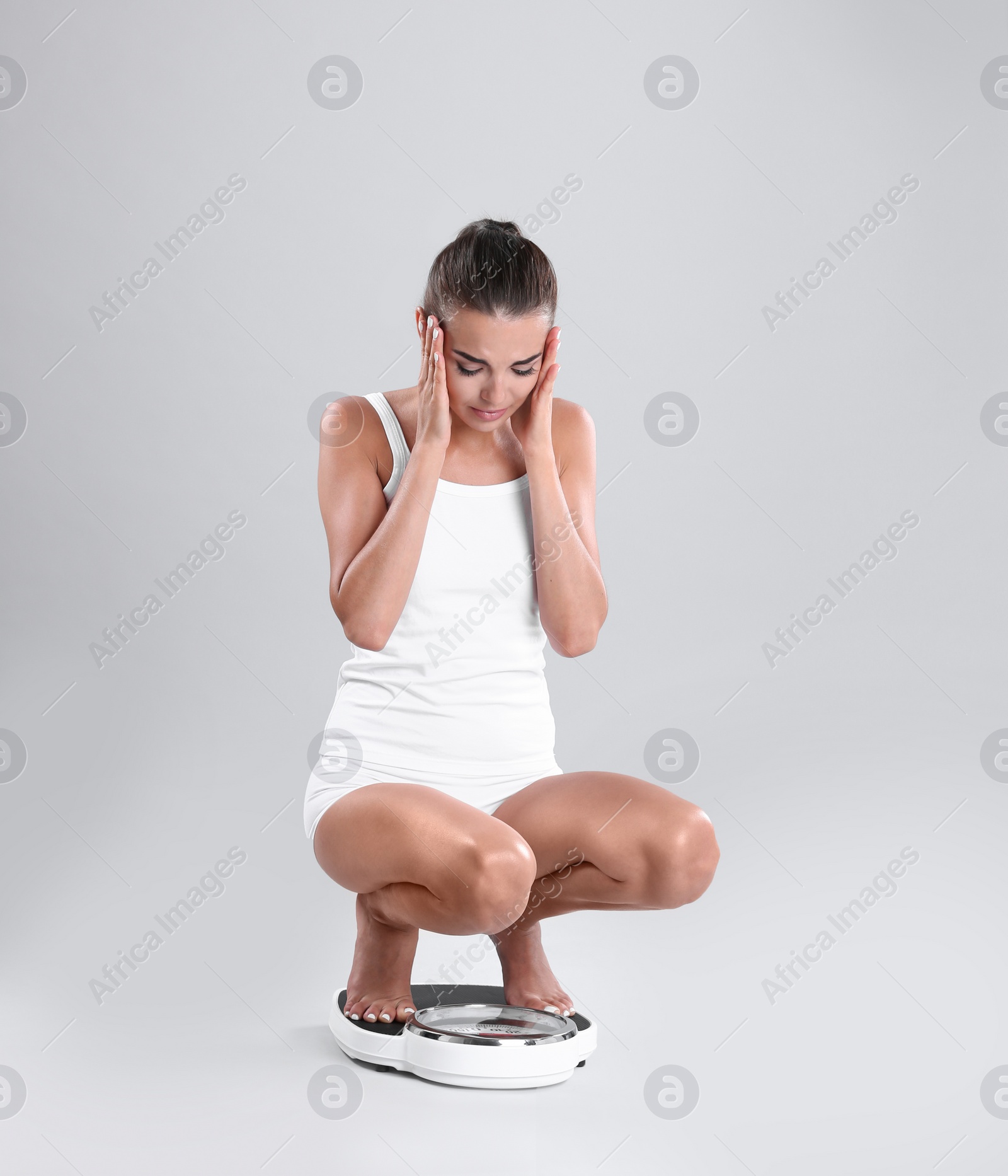 Photo of Unhappy young woman measuring her weight using scales on color background. Weight loss motivation