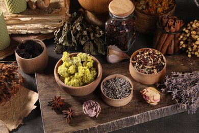 Photo of Many different dry herbs, flowers and spices on dark grey table