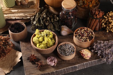 Many different dry herbs, flowers and spices on dark grey table