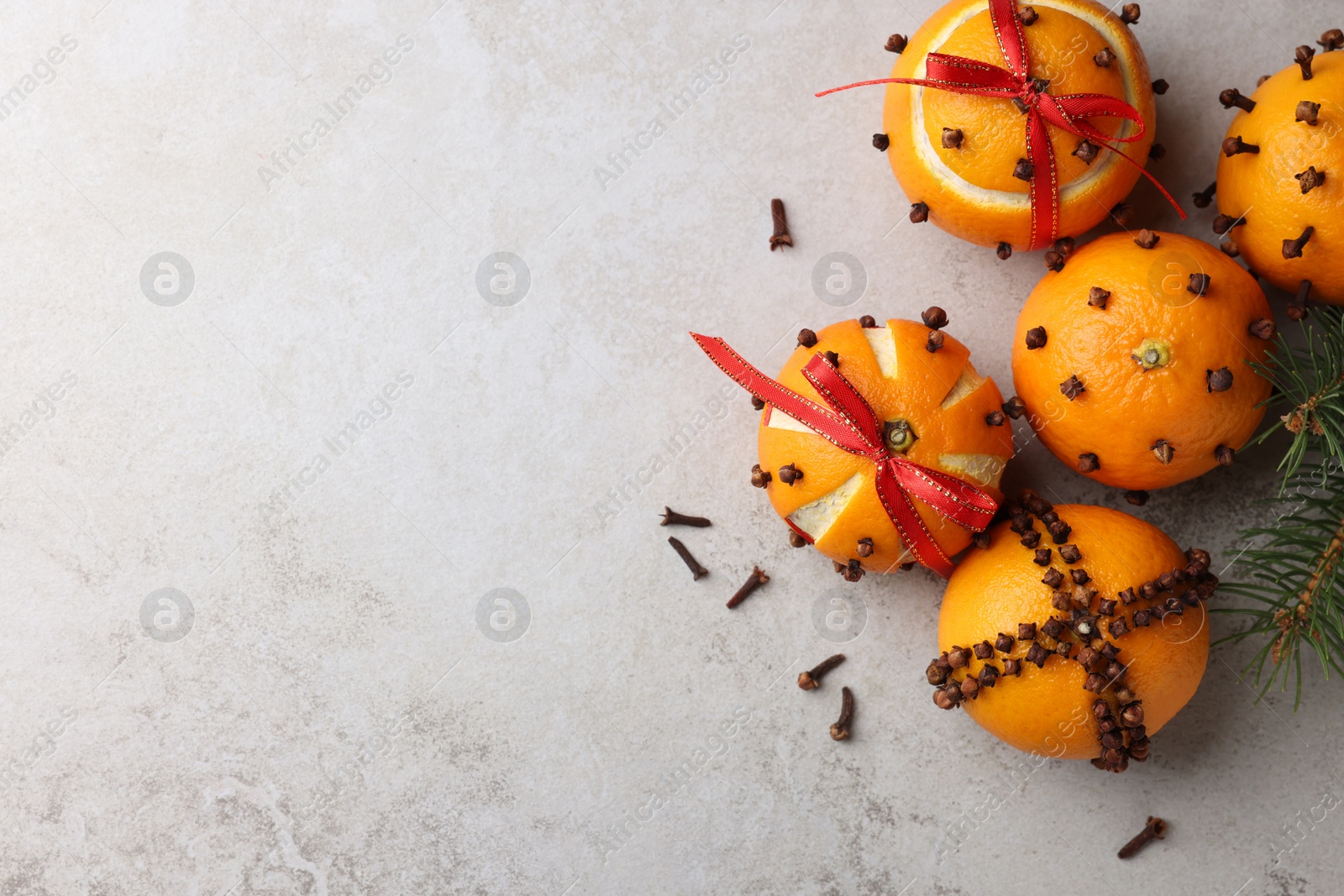 Photo of Pomander balls made of tangerines with cloves and fir branch on grey table, flat lay. Space for text