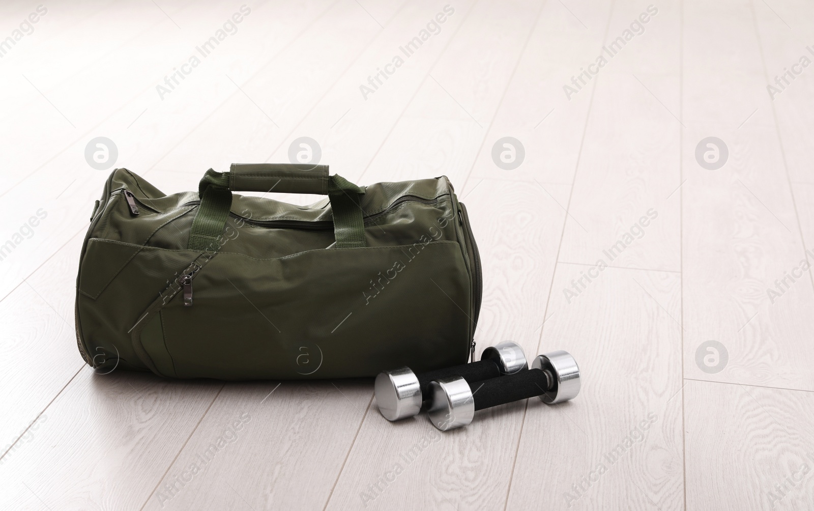 Photo of Sports bag and dumbbells on white floor, space for text