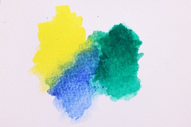 Blots of bright watercolor paints on white paper, top view