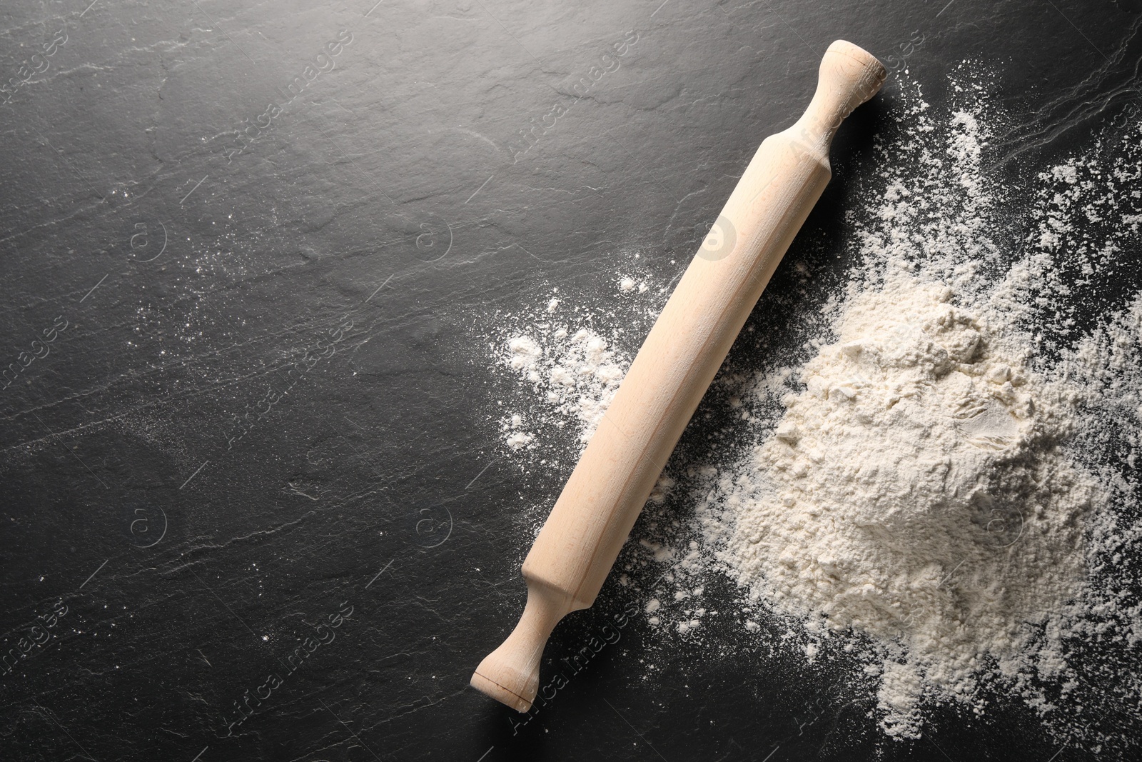 Photo of Pile of flour and rolling pin on black textured table, top view. Space for text