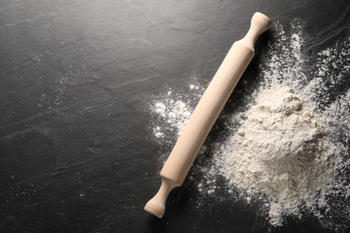 Photo of Pile of flour and rolling pin on black textured table, top view. Space for text